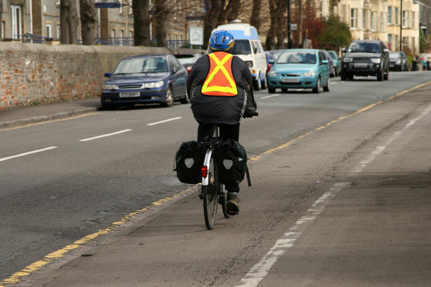 A photo of a cyclist wearing a reflective vest and helmet as he goes down a bike lane.