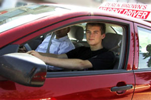 A young man student driver is learning to drive from a Class 5 Basic Driving course instructor.